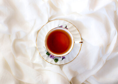 Top view of a cup of black tea in a fine china tea cup sitting on white fabric