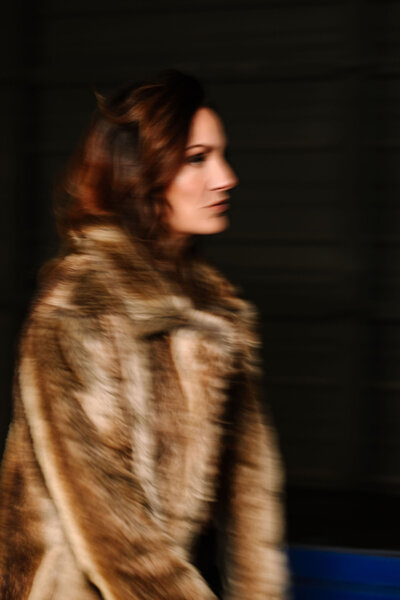 Blurry artistic side portrait of Juliet Trnka in a fur coat with a dark background