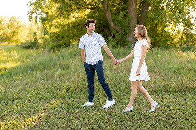 A white couple holding hands and walking outside in the grass