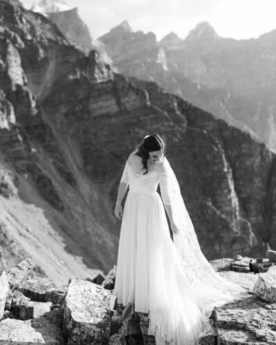 This stunning portrait captures the bride looking down at her dress after arriving by helicopter at a remote mountain location in Banff National Park. The breathtaking alpine setting enhances the elegance and beauty of the moment, creating a timeless image on her special day.