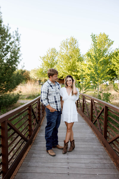 Couple wearing cowgirl and cowboy boots celebrating their engagement on a local wooden bridge in rural MN
