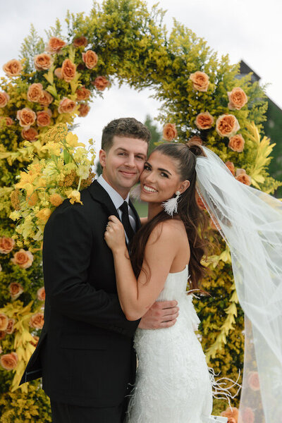 Bride and groom hug in front of a luxury floral display
