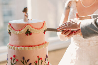 Hands cutting pink wedding cake