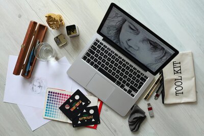 a desk covered in graphic design tools like a laptop color chart sketching tools and paper