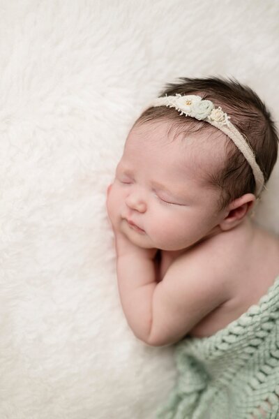 sleeping newborn baby posed on cream soft blanket with delicate floral headband and teal blanket