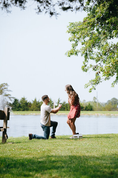 man kneeling to propose to girlfriend by lake