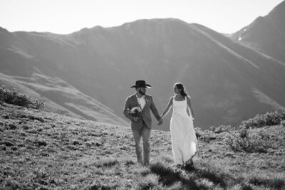 colorado elopement planning guide - bride and groom hold hands and run through the mountains during elopement wedding