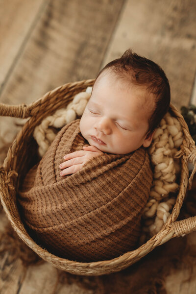 baby boy swaddled in a brown blanket in a wooden basket