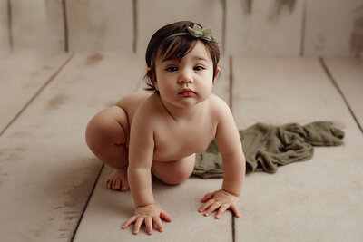 a one year old girl crouching on a wooden backdrop in a studio