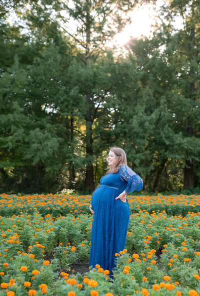 The profile of a expectant mother wearing a beautiful blue dress while standing in a field of flowers during a maternity session.