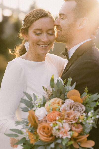 groom kisses brides temple in a golden sunlight moment creating a romantic scene