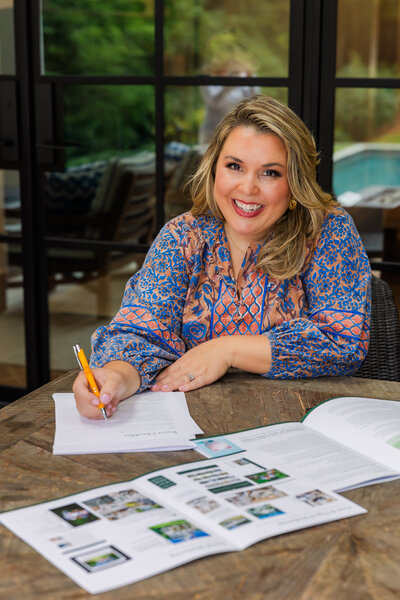 women wearing a pink and blue dress with patterns working at a patio table with paper, pen and brochure during branding with Laure Photography Atlanta