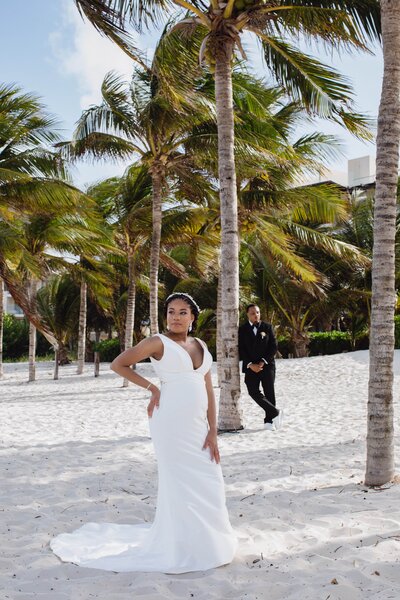 A bride and groom posing in front of palm trees on the beach.
