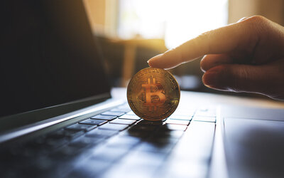 bit coin balanced by finger on laptop keyboard