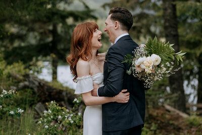 A bride and groom wearing a yellow and green puffy jacket hold each other on top of Rainbow Glacier in Whistler. There is snow all around and blue skies.