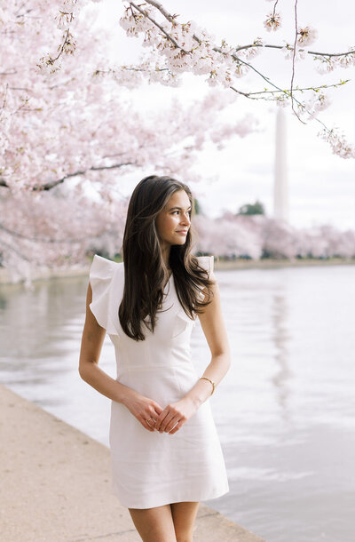 Grad girl poses by tidal basin in DC with cherry blossoms and Washington Memorial in background