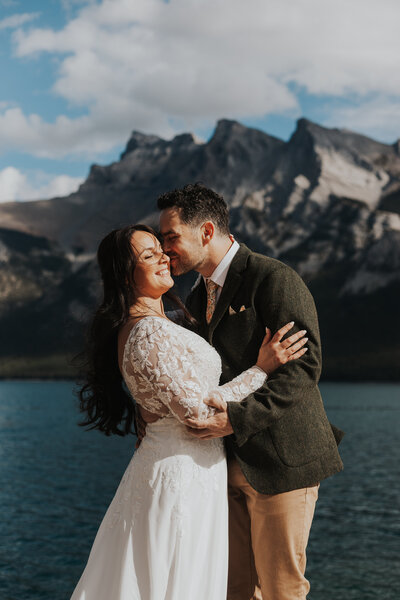 A bride and groom kiss with the mountains in the background in Banff National Park