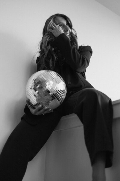 Black and white image from a low angle of a woman holding a disco ball wearing a power suit