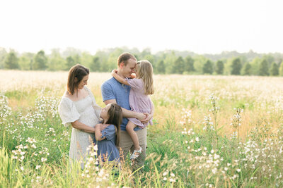 Family of four standing in a beautiful field smiling at each other