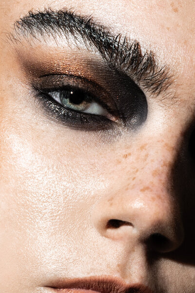 Extreme beauty close-up of freckled model with dramatic lighting and rusty eyeshadow