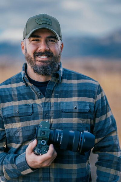Portrait of Joseph Mayden, veteran-owned Montana photographer and cinematographer, smiling outdoors with camera gear, showcasing his professional and approachable style.