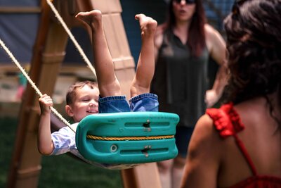 Exuberant child on a swing with family cheering, captured by a Connecticut Documentary Family Photographer in a backyard setting.