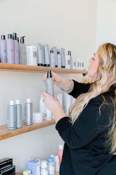 Ingrid arranging professional beauty products on salon shelf at Lavender & Ink Studios