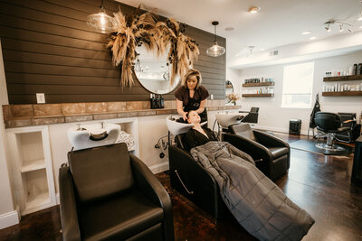 Sara Carter, founder and stylist at Maven + Grace Salon, smiling and seated in her light-filled studio space in McMinnville