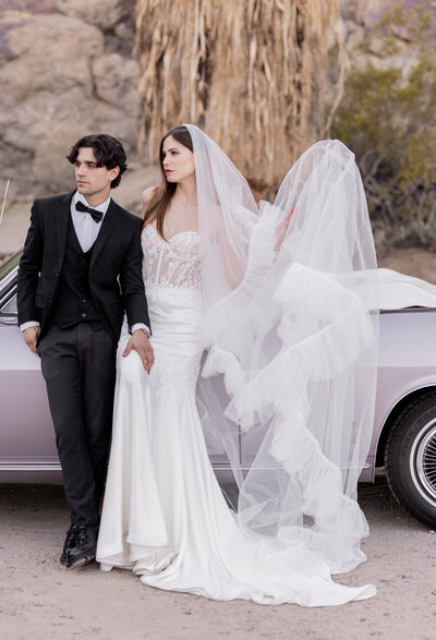 An effortlessly chic bride and groom strike a modern yet timeless pose in the Palm Springs desert. With a vintage convertible and a flowing couture veil, this fine art wedding portrait captures romance, style, and cinematic elegance.