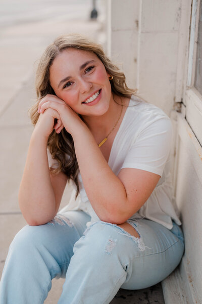 Girl smiles with her face resting against her hands.
