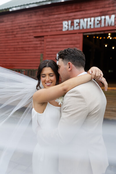 Veil shot of bride and groom snuggling close together in front of a barn door