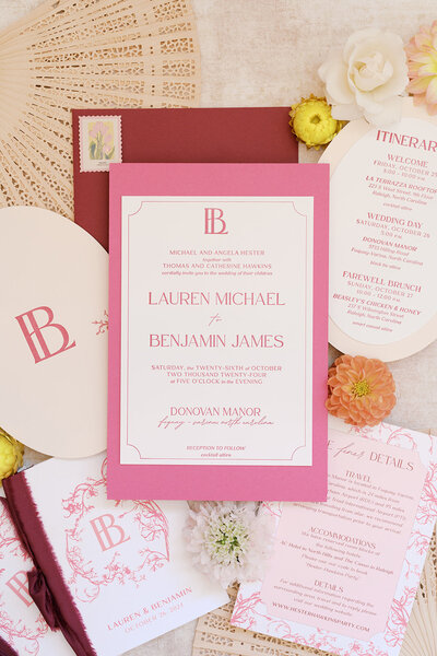 Vibrant wedding invitation suite featuring layered fuchsia and blush pink cardstock, custom monogram, floral line illustrations, itinerary fan, and coordinated insert cards. Styled with fan accents, floral blooms, and wax seals—ideal for a romantic, colorful, and thoughtfully designed wedding celebration at Donovan Manor.