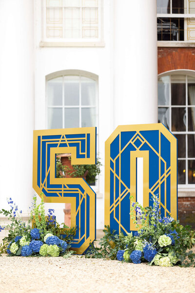 6ft freestanding blue and gold art deco style 50 sign with blue and green flower base outside avington park for a birthday party