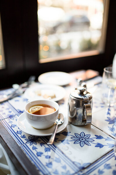 Cup of tea with a slice of lemon on a saucer sitting on a blue tiled table