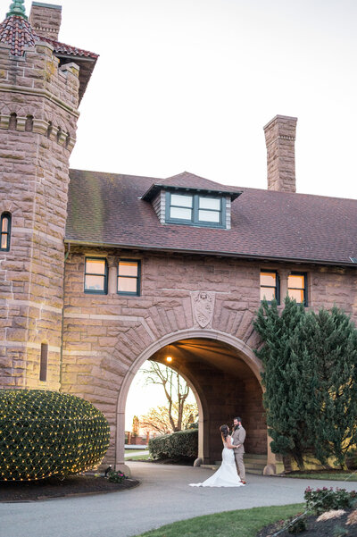 A bride and groom share a romantic moment under the grand stone arch at Oceancliff’s historic estate in Newport, surrounded by timeless architecture and coastal charm.