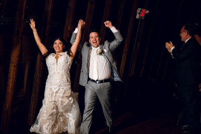 A bride and groom throw their hands up at their reception.