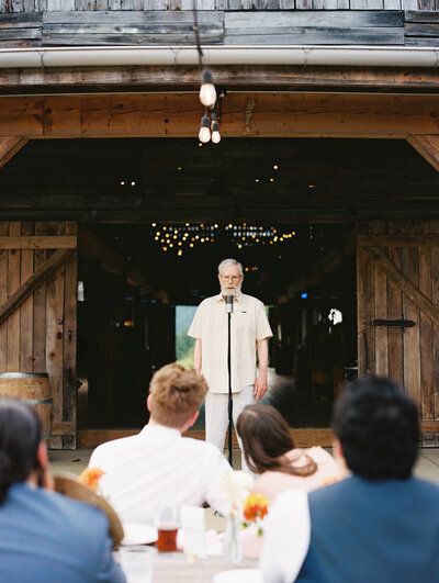 The bride and groom listen to a speech given from the barn porch at Paint Rock Farm, a scenic wedding venue in North Carolina, captured by My Sun and Stars Co.