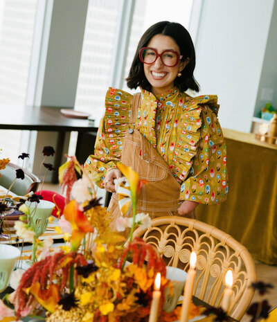 A female posing for the camera wearing a yellow dress and oversized red glasses at a dinner hosting