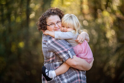 mother with curly hair and plaid shirt hugging toddler blond daughter