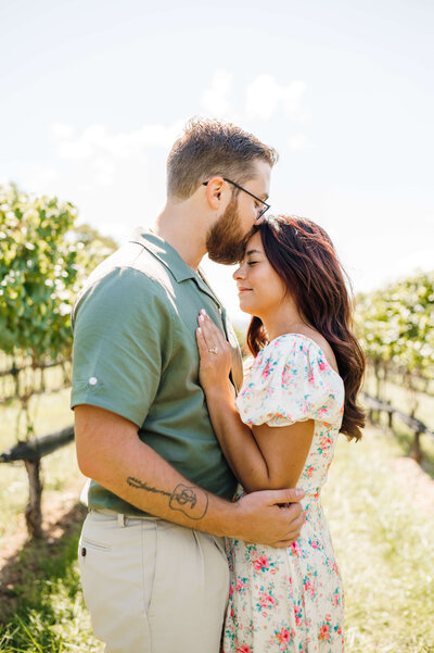 Leesburg VA engagement photos with man and woman embracing while the man kisses the top of the womans head as she rests her hands on his chest in a vineyard