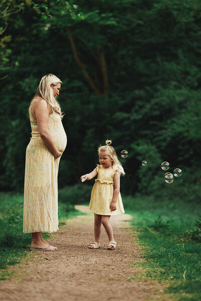 Zwangere moeder met meisje die bellen aan het blazen is alle 2 in een gele jurk