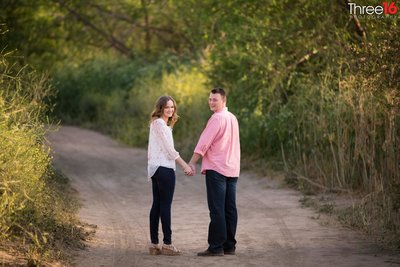 Groom to be embraces his fiance from behind as they sit on a large rock in a rock pile at Carbon Canyon Regional Park in Brea, CA