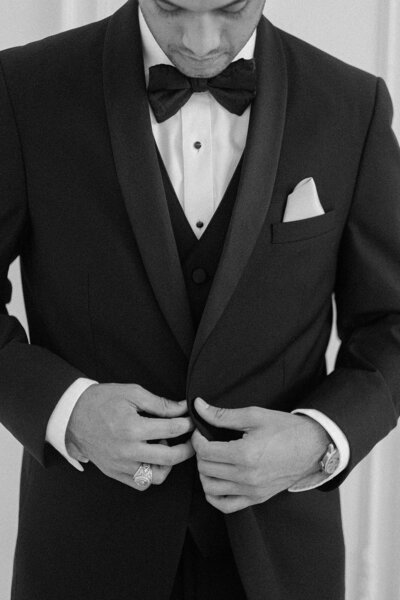 black and white image of groom buttoning jacket