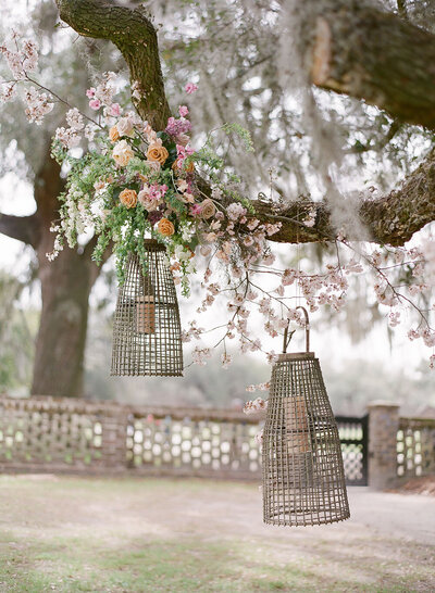Woven lanterns suspended from a tree for unexpected garden wedding decor with composition from Floressence