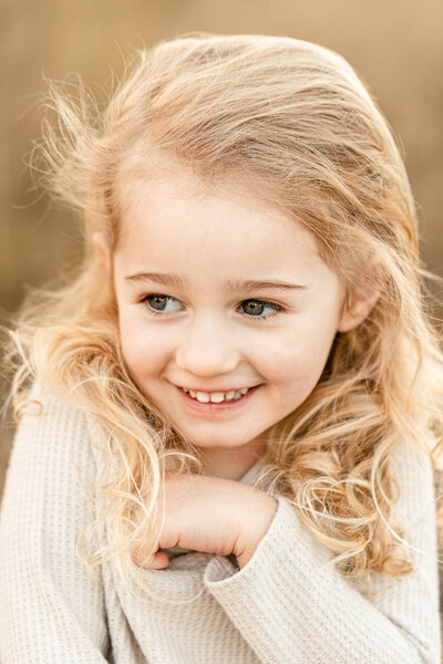 Little blonde girl wearing a cream waffle knit shirt and smiling off camera. Portland Family Photo session.