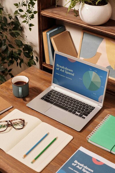 Office setup showcasing a laptop with a professional presentation for Google Ads management services. The wooden desk includes an agenda, pen, glasses, cup of coffee, and some books, highlighting a well-organized and professional workspace.