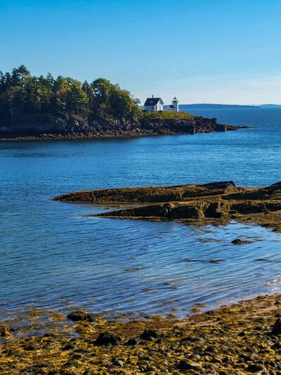 A secluded coastal lighthouse on the rocky shores of Maine, surrounded by calm blue waters | theViatrix Personalized Travel Planning