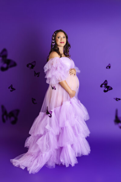 Maternity Photographer, a n expectant mother wears a purple dress before a backdrop of butterflies