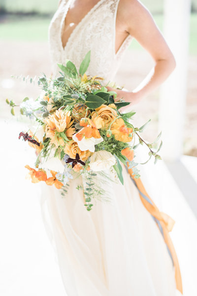 Beautiful bride in wedding gown holds lush orange and green bouquet