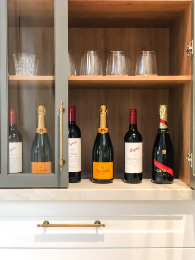 A bespoke cabinet beautifully displays five wine bottles and six glasses on its shelves, reflecting the elegance of custom interior design in Newcastle.